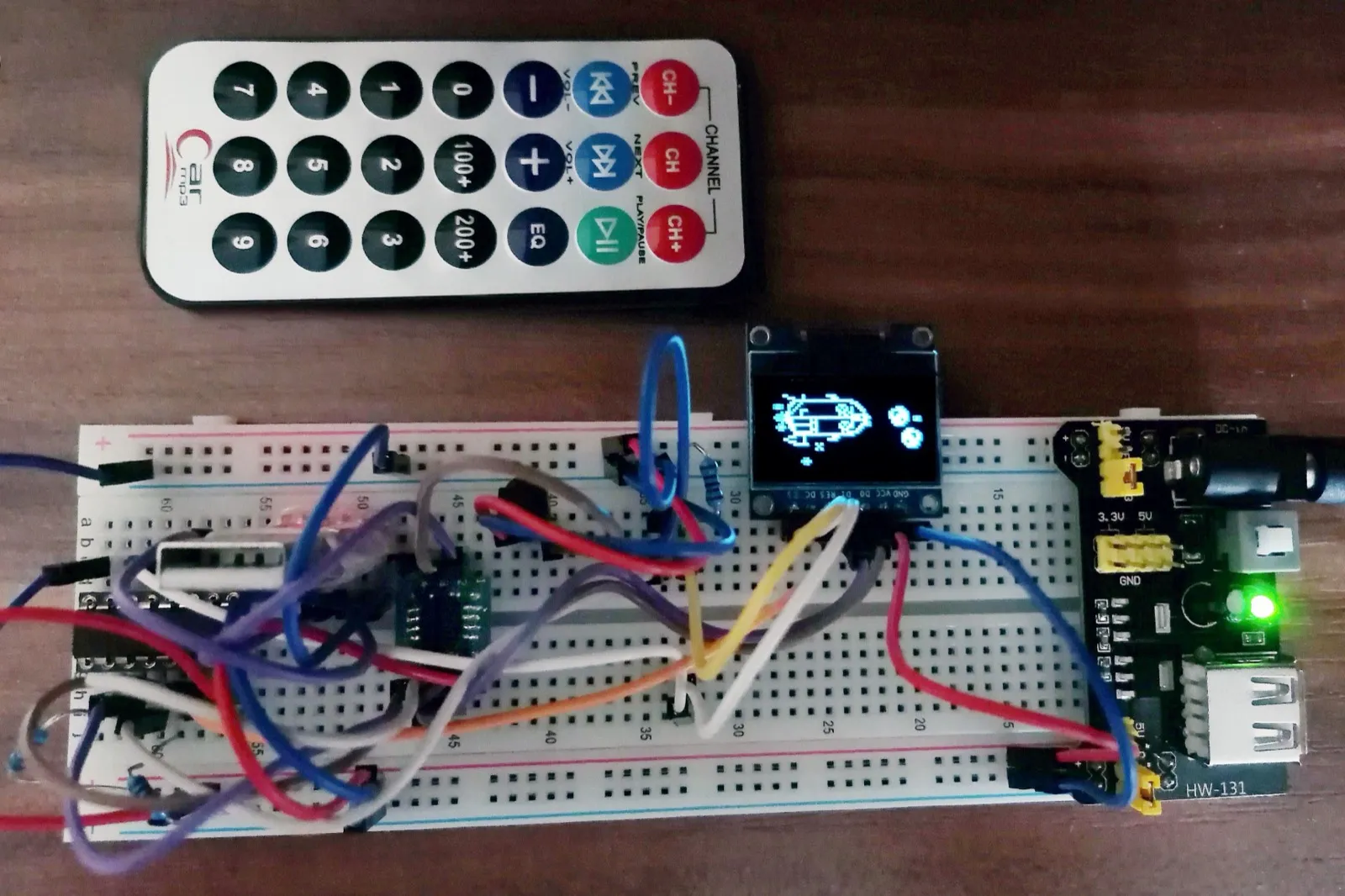 A breadboard threaded with jumper wires, carrying the ATtiny85, an IR receiver, a power module, and the OLED mid-game, with a small remote beside it